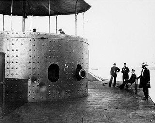 Several people standing next to gun turret of USS Monitor.