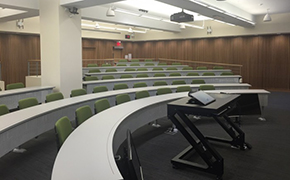 Five curved rows of fixed seating with green chairs facing a lectern.