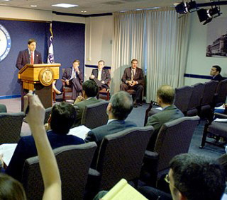 A speaker gives a press conference in a crowded room.