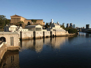 a photograph showing a canal lined with Greek revival style buildings, and showing the Philadelphia skyline in the background.