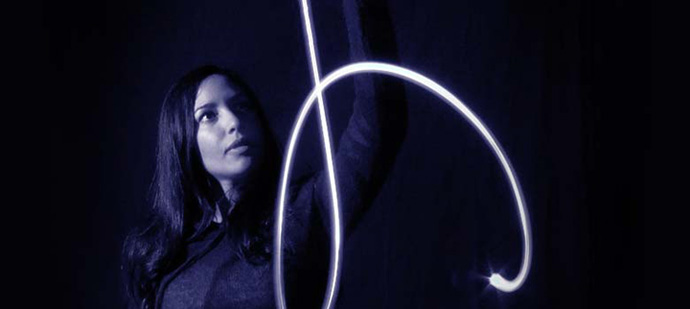 A photo of a woman and a beam of blue light in the dark.