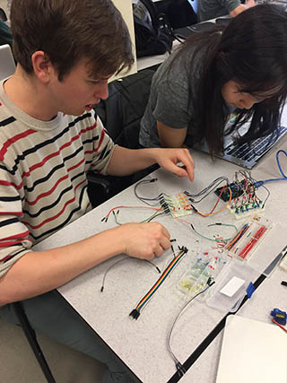 Two students connecting wires and circuits, working on their electronic prototyping project