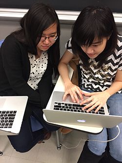 Two women in a classroom setting looking at one laptop screen.